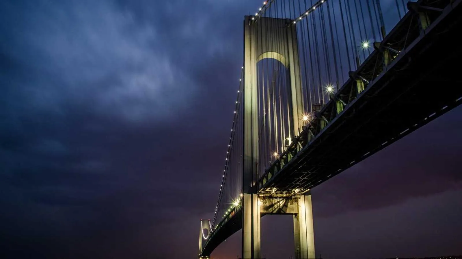 A suspension bridge lit up at night against a dark blue sky