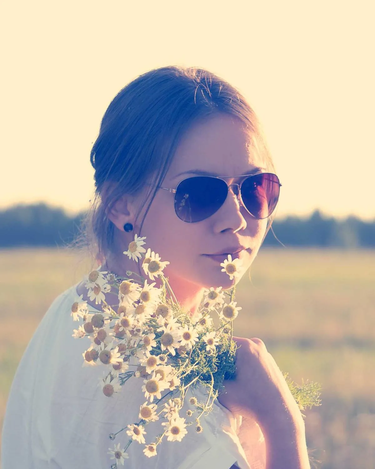 A woman in aviator sunglasses holding wildflowers in a sunlit field